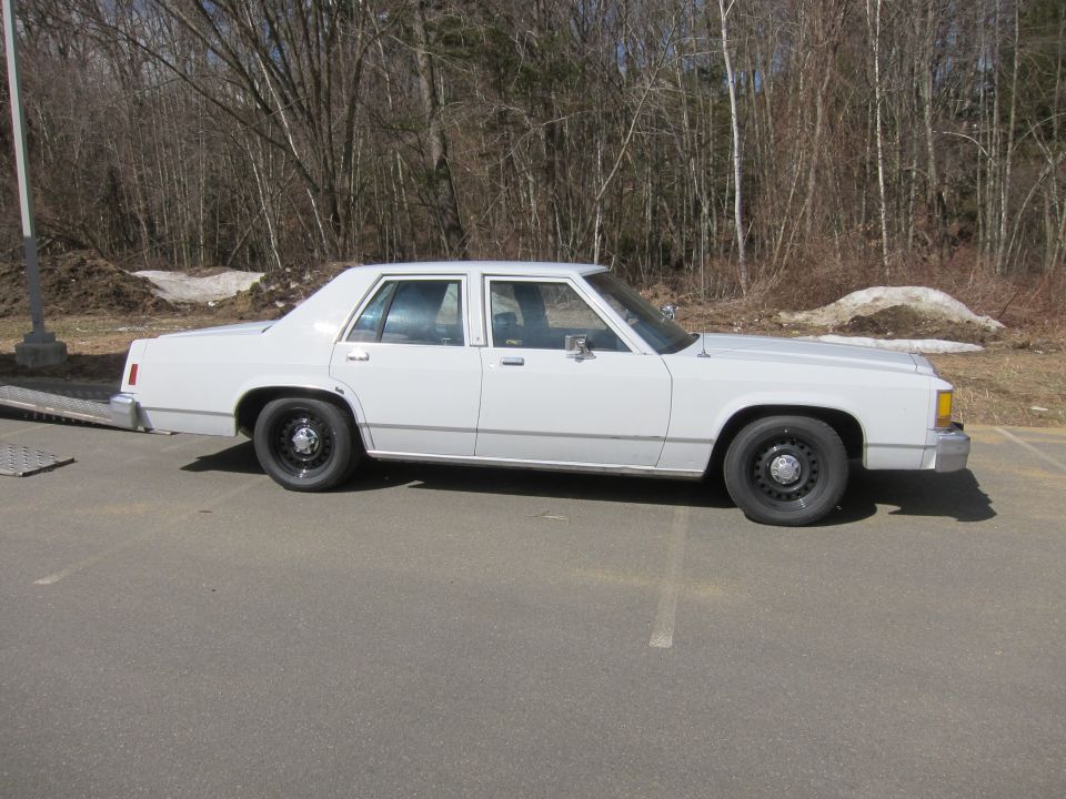 White sedan parked on asphalt, side view. Features black wheels and chrome trim