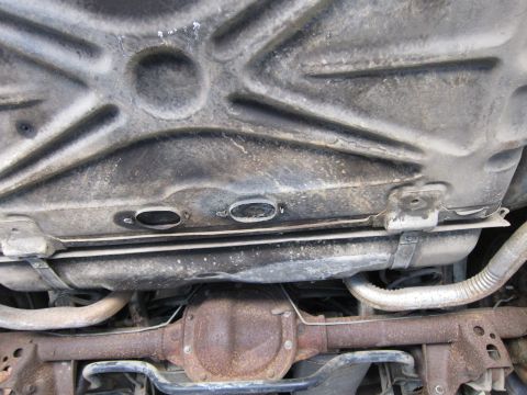 1991 Ford LTD Crown Victoria - The underbody of a vehicle, revealing its fuel tank, exhaust system, and rear differential, with visible dirt and rust.