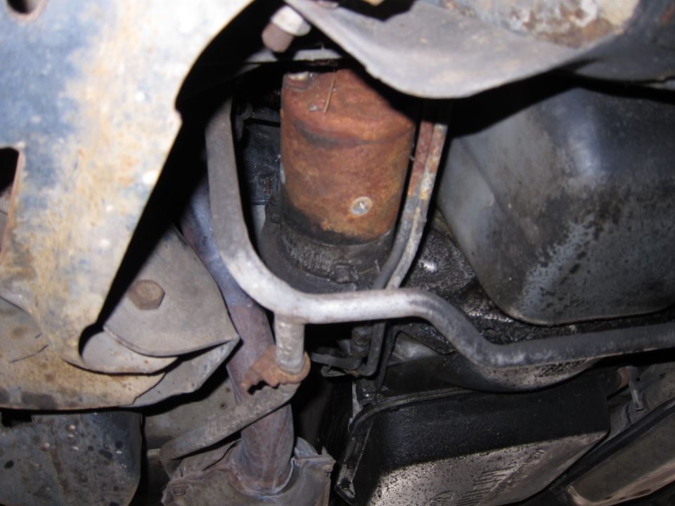 Underside of a vehicle showing rusty metal components, oil pan, and exhaust pipe