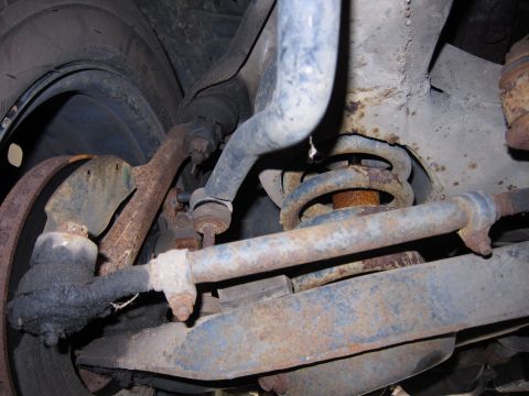 1991 Ford LTD Crown Victoria - Close-up view of heavily rusted vehicle suspension components, including a tie rod and coil spring.