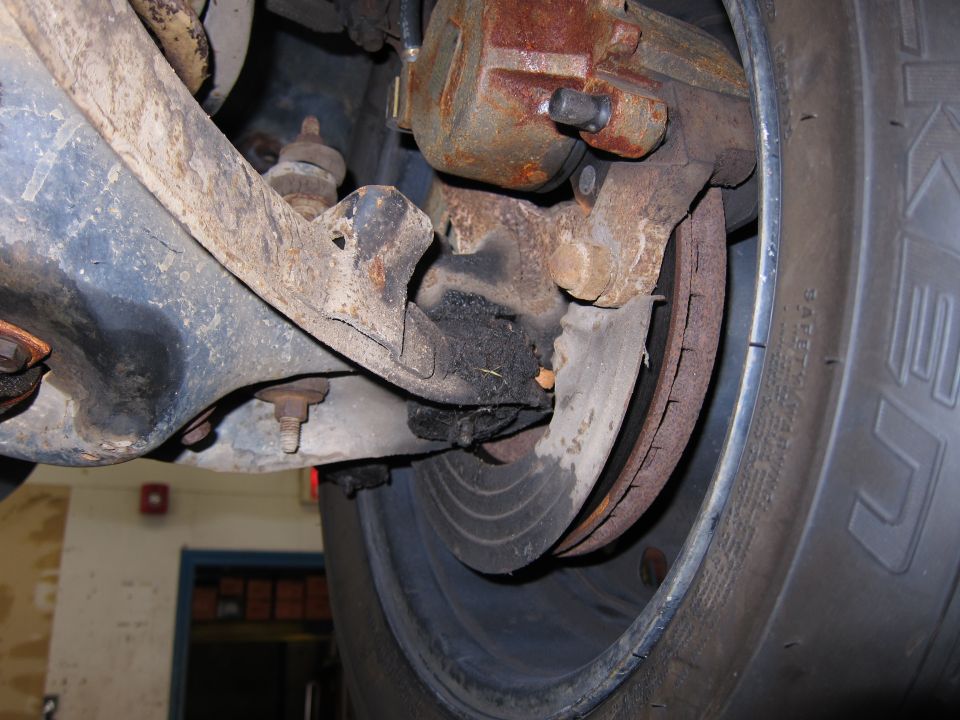 close-up of rusted brake caliper, rotor, and suspension components