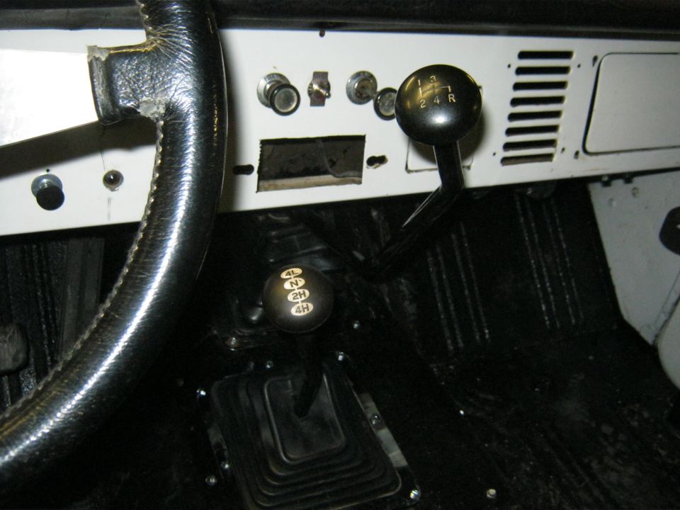 Interior shot of a vehicle's dashboard, showing a steering wheel, two gear shifters, and various switches