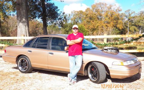 1993 Ford Crown Victoria - A man poses with a modified 1993 Ford Crown Victoria a prominent hood scoop and aftermarket wheels.