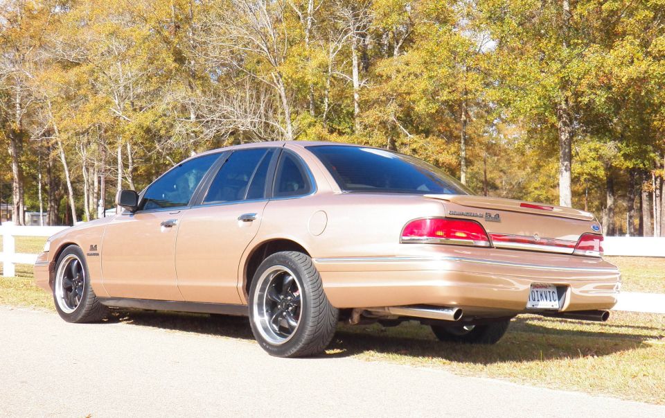 Rear view of a tan Ford Crown Victoria with aftermarket wheels. It has a spoiler and dual exhaust