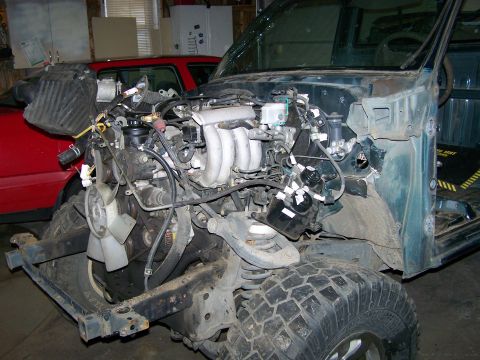 1988 Suzuki Samurai - The engine and front chassis of a vehicle are shown, with a red vehicle in the background and a SuperMotors logo at the bottom.