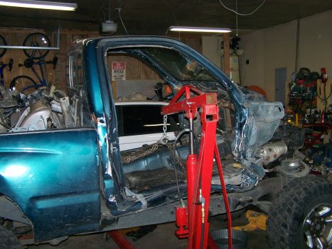 1988 Suzuki Samurai - Disassembled teal pickup truck in a garage, with an engine hoist supporting the front section.