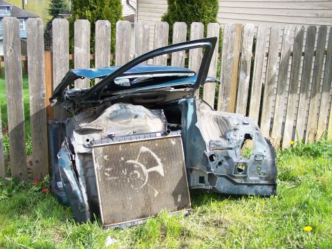 1988 Suzuki Samurai - The front end of a heavily damaged vehicle, including the radiator, sits in a grassy yard next to a fence.