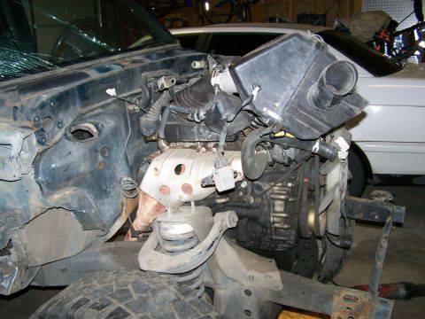 1988 Suzuki Samurai - The engine bay and front section of a vehicle are visible, with a broken windshield and a large air intake box.