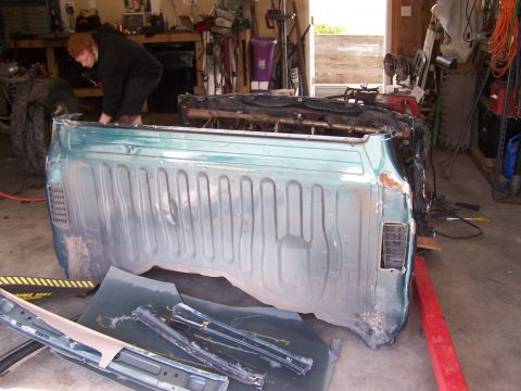 1988 Suzuki Samurai - A person works on a teal-colored pickup truck bed in a cluttered garage setting.