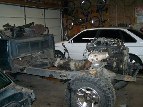 1988 Suzuki Samurai - A truck chassis is in a garage, with an engine and transmission mounted, and another vehicle body nearby.