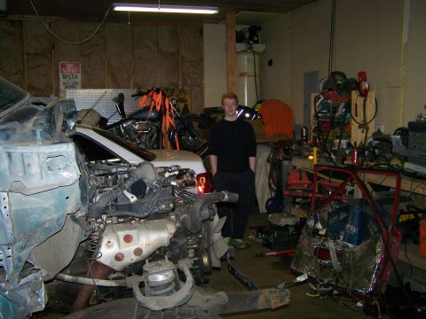 1988 Suzuki Samurai - A person stands in a cluttered garage next to a disassembled vehicle's engine and chassis.