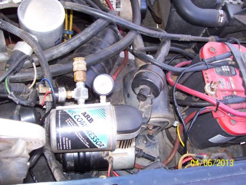 1990 Ford Bronco - Close-up of an ARB air compressor and gauge installed in a vehicle's engine bay, showing various hoses and wiring.