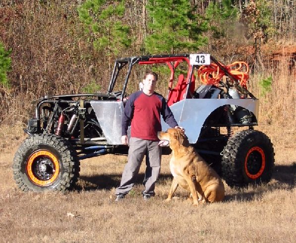 Man and dog beside a black tube-frame rock buggy with aluminum panels and number 43 plate