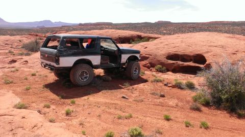 1994 Ford Bronco - A modified Ford Bronco navigates a desert landscape with its doors ajar.