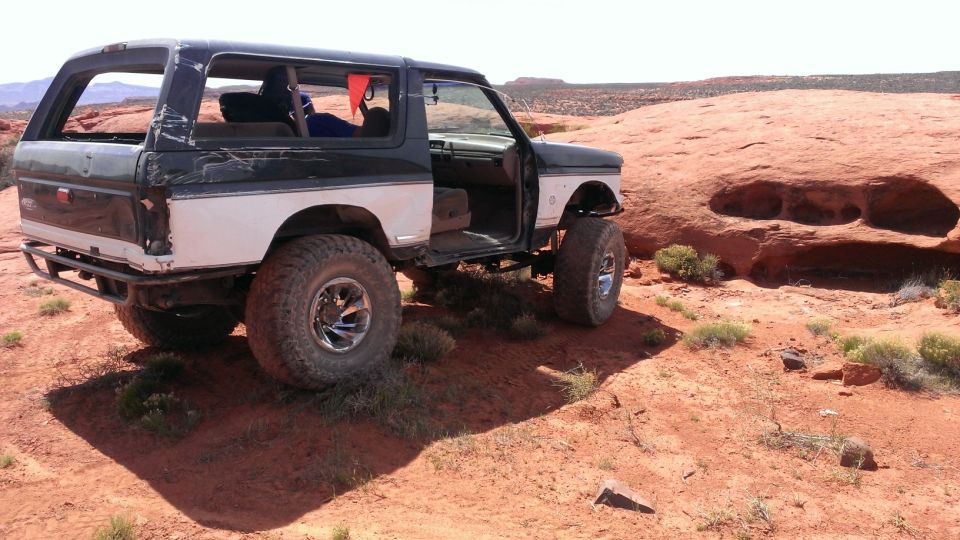 Modified Ford Bronco with aftermarket bumper and large tires parked on red rock terrain