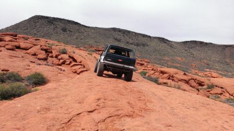 1994 Ford Bronco - A 1994 Ford Bronco navigates a steep, rocky incline in a desert landscape.