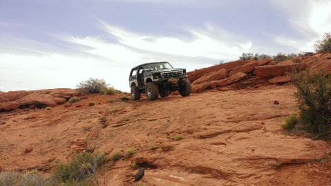 1994 Ford Bronco - A lifted Ford Bronco navigates a steep, rocky incline under a cloudy sky.