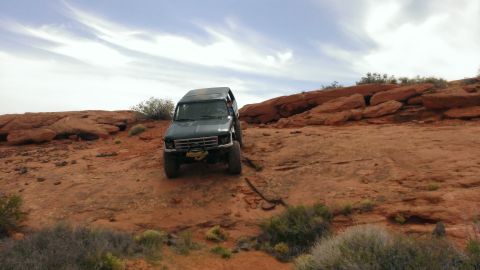 1994 Ford Bronco - A dark green Ford Bronco navigates a , off-road terrain under a cloudy sky.