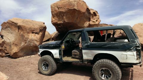 1994 Ford Bronco - Modified Ford Bronco with doors removed parked near large rocks in a desert landscape.