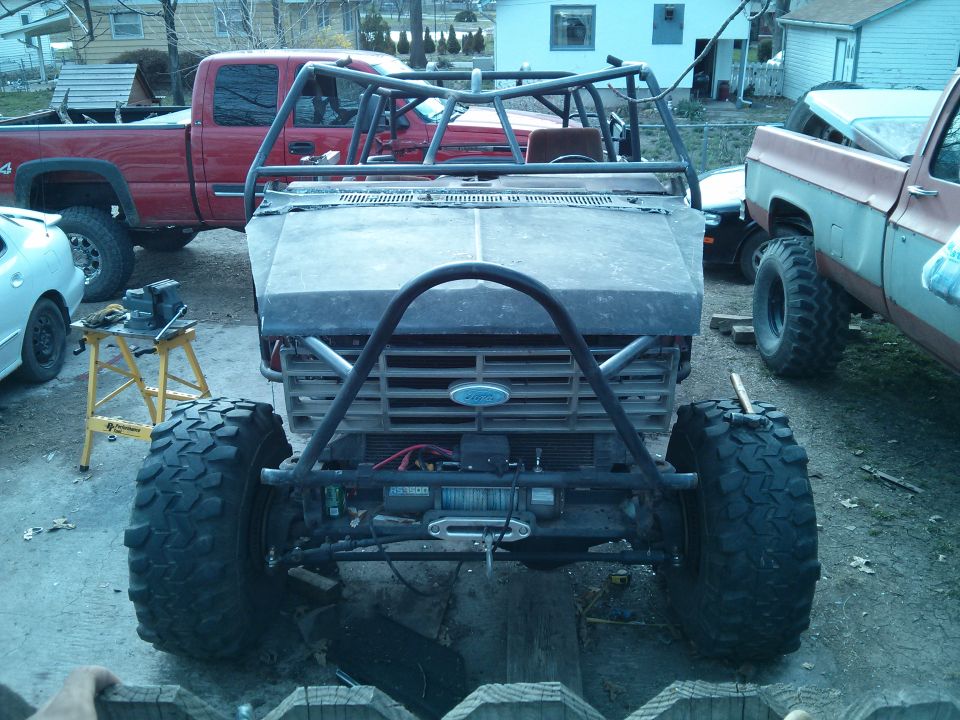 Modified off-road vehicle with roll cage, winch, and large tires. Ford emblem visible on grille