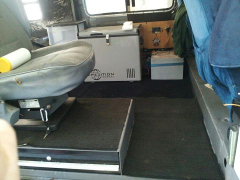1988 Ford E350 - Interior view of a van, showing seats, a portable refrigerator, and storage containers.
