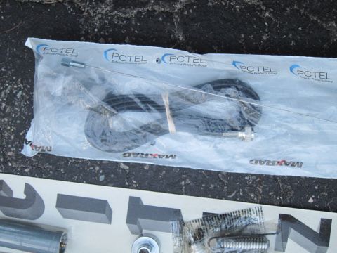 1991 Ford LTD Crown Victoria - Unopened MAXRAD antenna parts, including a coiled black cable and a thin metal rod, are displayed on a dark, textured surface.