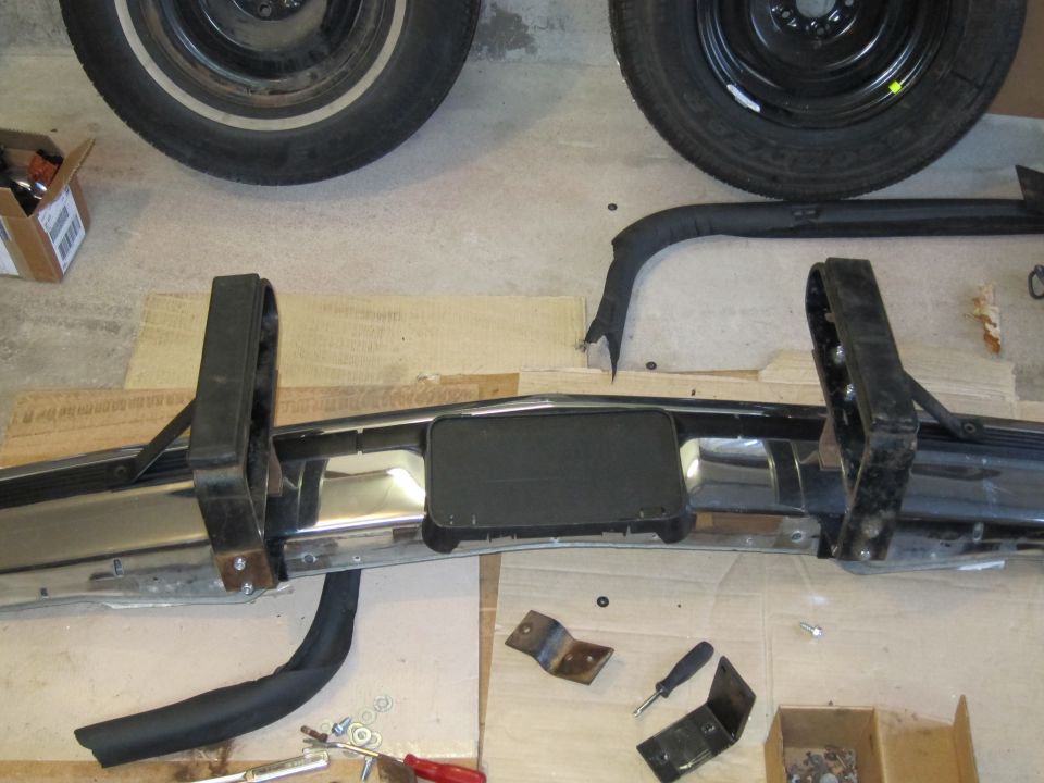 Chrome bumper with black rubber trim and license plate bracket, two tires visible above
