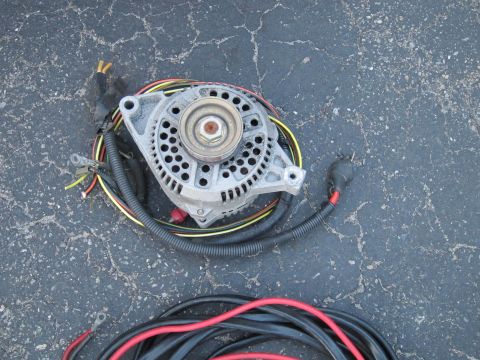 1991 Ford LTD Crown Victoria - An alternator with its wiring harness lies on a cracked asphalt surface.