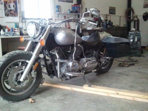 1995 Ford F-150 - Motorcycle with a bare metal fuel tank and saddlebags is on wooden ramps in a garage.