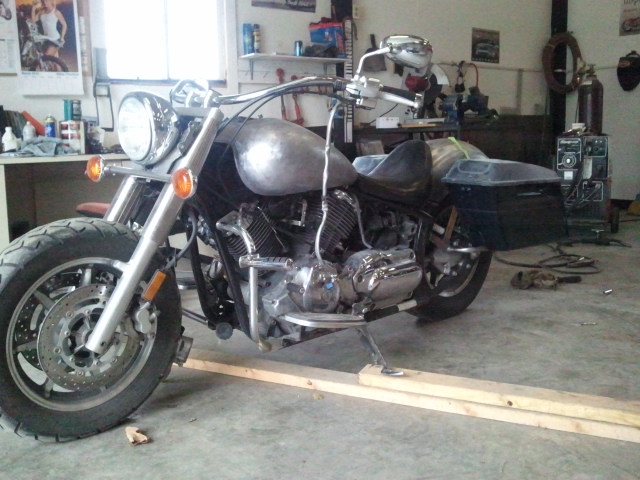Motorcycle with a bare metal fuel tank and saddlebags, on wooden ramps in a garage
