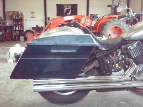 1995 Ford F-150 - Side view of a motorcycle's saddlebag and exhaust pipes, with a tractor in a workshop setting that appears to be a workshop.