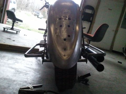 1995 Ford F-150 - This custom motorcycle features a raw metal fender and dual exhaust pipes, with a workshop environment visible in the background.