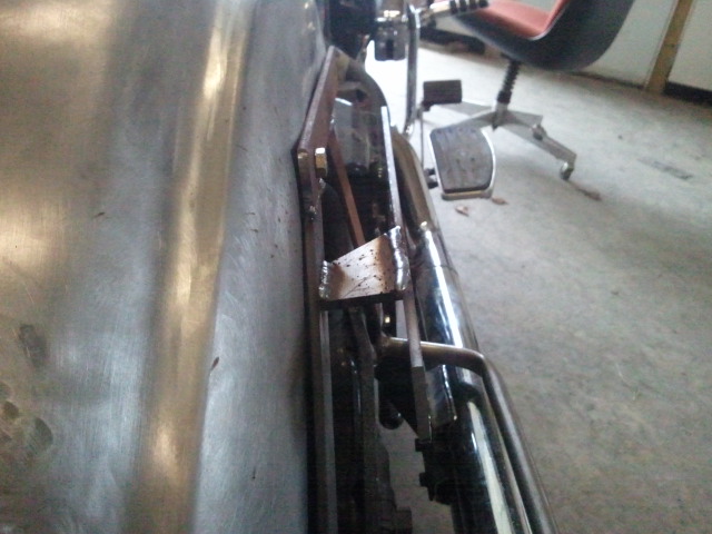 Unfinished metal panel on a vehicle side with chrome exhaust pipe and mechanical parts visible