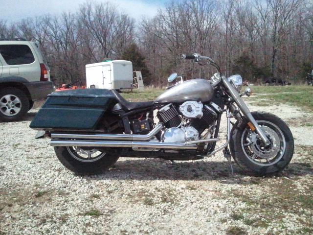 Custom cruiser motorcycle with saddlebags and dual exhaust pipes parked on gravel
