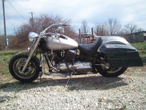1995 Ford F-150 - A motorcycle with a metallic fuel tank and large black saddlebags sits on a gravel surface outdoors.
