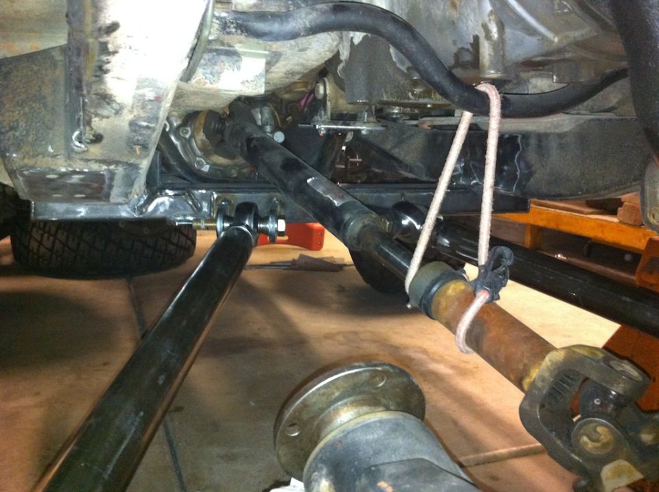 Undercarriage of a vehicle showing a differential, driveshaft, and suspension links. A rope is tied around a driveshaft