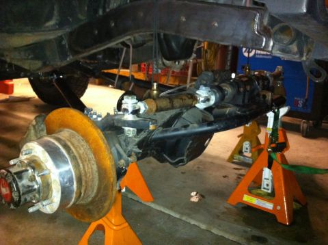 1987 Suzuki Samurai - Close-up view of front axle and suspension components supported by jack stands in a workshop.