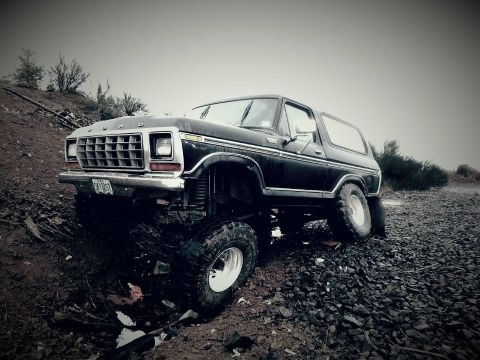 1979 Ford Bronco - A black Ford Bronco with a lifted suspension navigates a rough, rocky landscape.