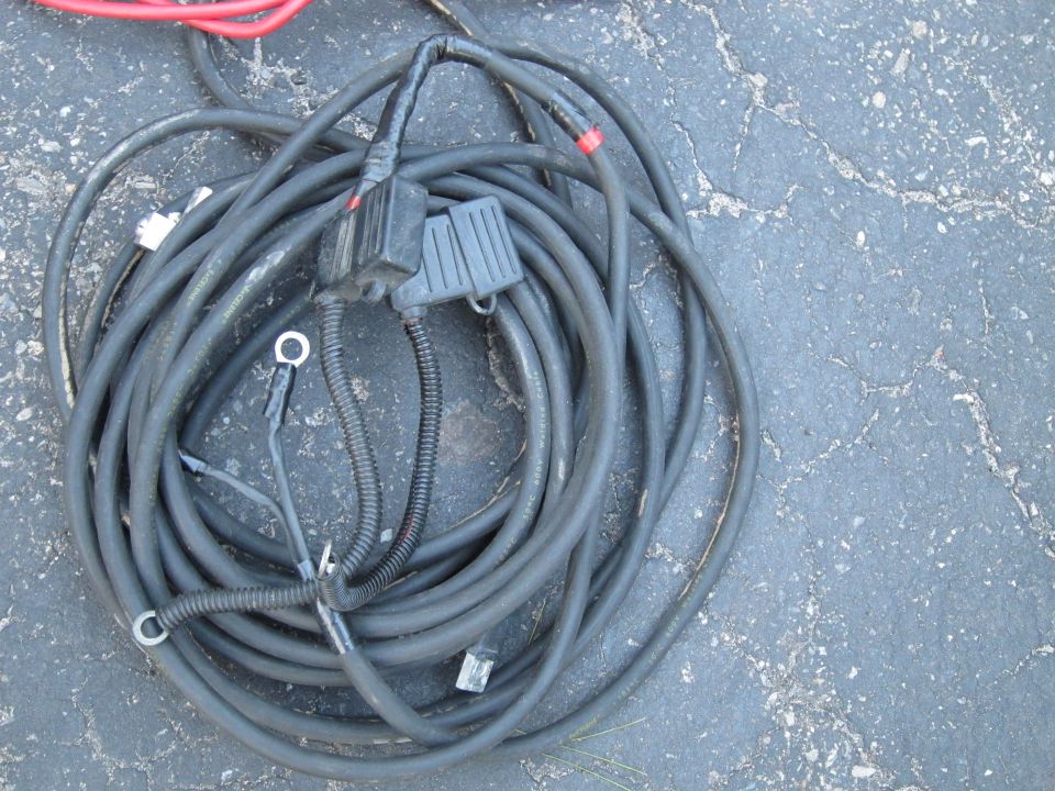 Tangled automotive wiring harness with black cables, connectors, and ring terminals on asphalt