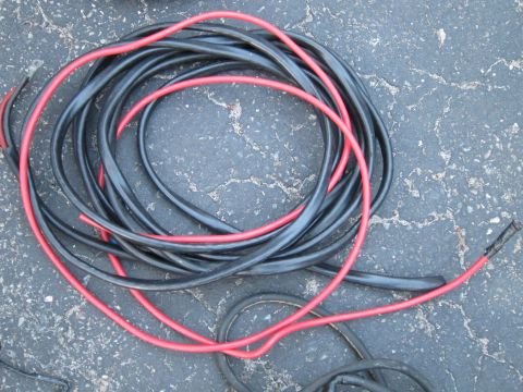 1991 Ford LTD Crown Victoria - A tangled mess of black and red electrical cables lies coiled on a cracked asphalt surface.