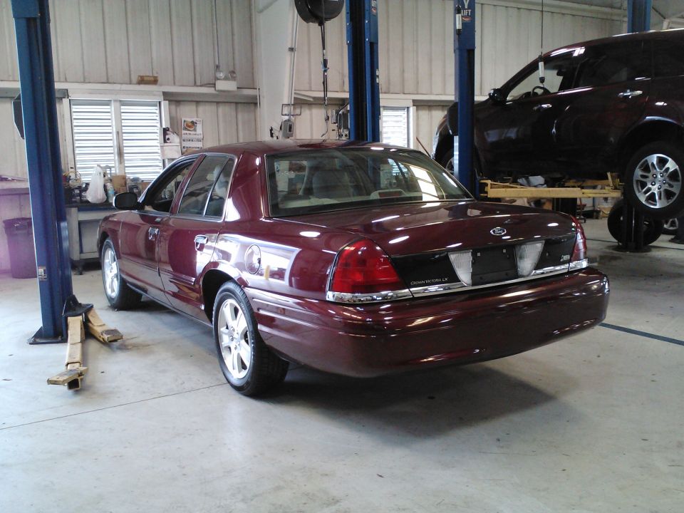 Maroon 2011 Ford Crown Victoria parked in a garage with another vehicle on a lift behind it