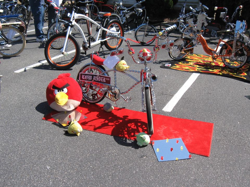 Custom lowrider bicycle with 'LOW RIDER' plate, red carpet, and Angry Bird plush toy. Other bicycles visible in background