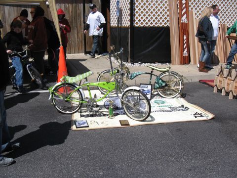 1994 Ford Bronco - A pair of custom lowrider bicycles are displayed on a mat resembling a giant dollar bill, with trophies and awards nearby.