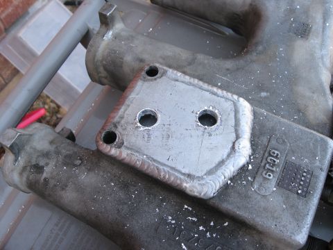 1981 Ford Bronco - A close-up shows a metal bracket with four holes and visible welding marks, alongside another metal component with a part number.