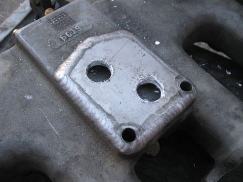 1981 Ford Bronco - Close-up of a metal part with visible welding and drilled holes, likely an intake manifold component.