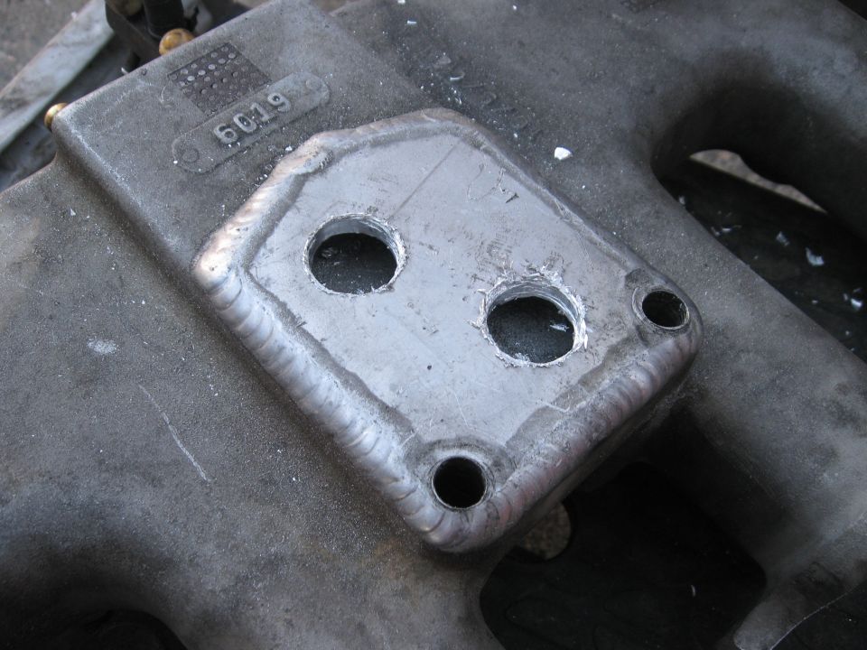 Metal intake manifold part with two drilled holes and welded plate