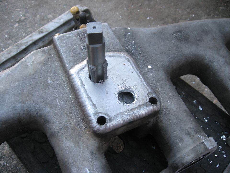 Close-up of an intake manifold with a tap tool inserted into a newly threaded hole