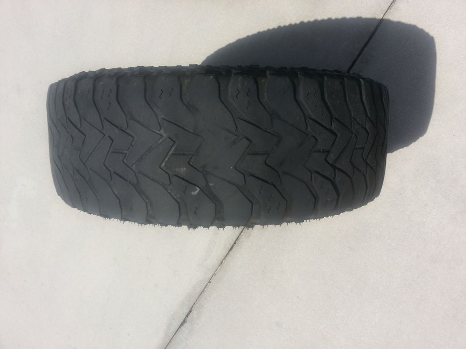 Tire with aggressive tread pattern, casting a shadow on a light-colored surface