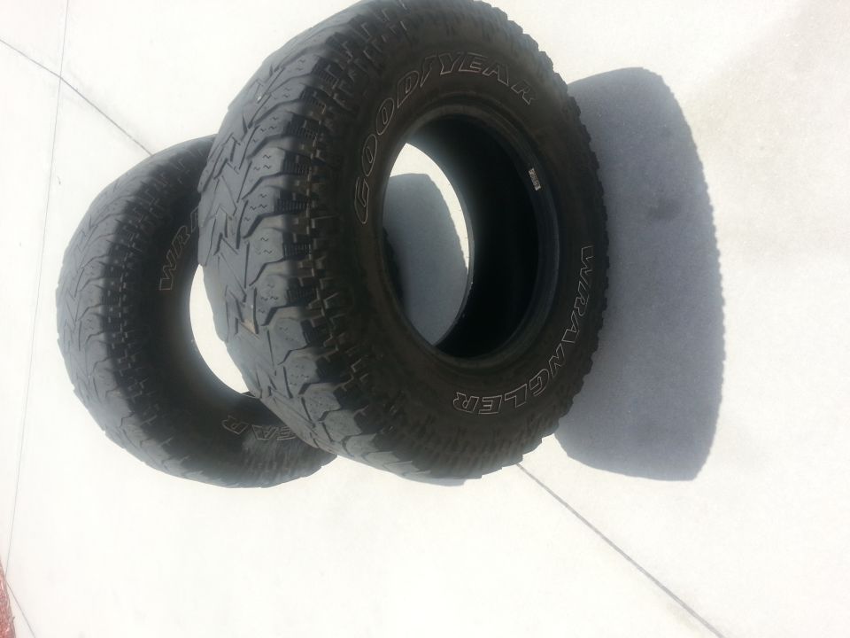 Two Goodyear Wrangler tires on a white surface, one partially obscuring the other