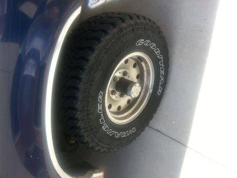 1994 Ford Bronco - Close-up of a Goodyear Wrangler spare tire mounted on the exterior of a blue vehicle.